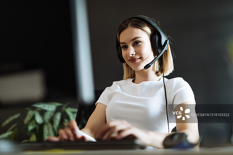 年轻的职业女性在呼叫中心用带耳机的台式电脑工作图片素材