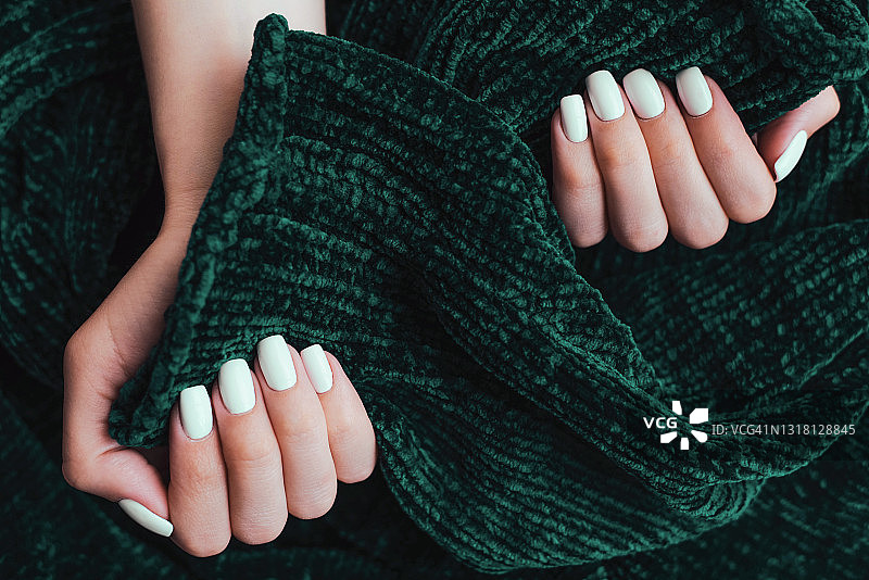 绿色丝绒背景上的白色美甲女性手部图片素材