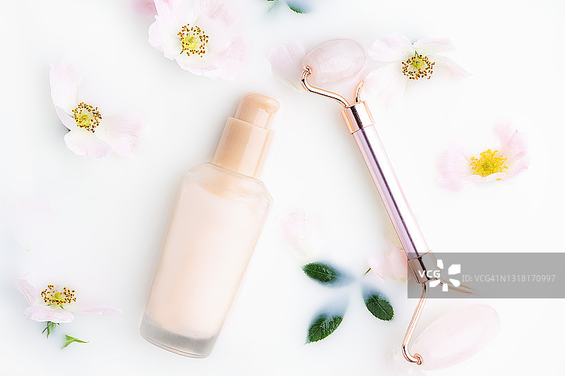 美丽的白色玫瑰花和粉色小瓶中的洁面乳或精华液，玫瑰石英面部滚轮在牛奶浴中图片素材