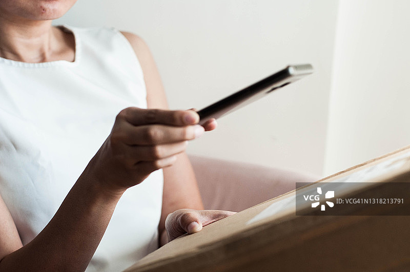 东南亚年轻女人用手机扫描纸箱条形码图片素材