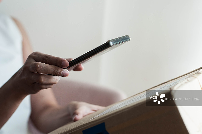 东南亚年轻女人用手机扫描纸箱条形码图片素材