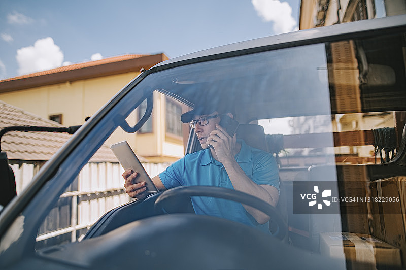 中国中年男性送货员在货车内用手机与顾客沟通图片素材