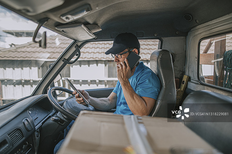 中国中年男性送货员在货车内用手机与顾客沟通图片素材