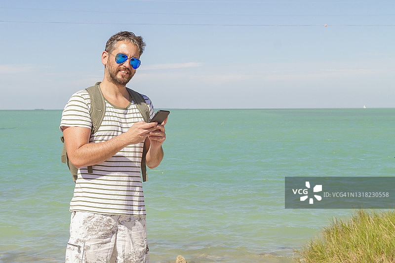 在佛罗里达州基韦斯特，在炎热的夏日阳光下用智能手机发短信的年轻男人图片素材