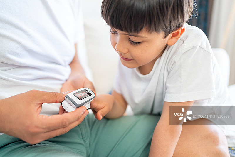父亲用指尖脉搏血氧仪检测儿子的血氧饱和度和脉率图片素材