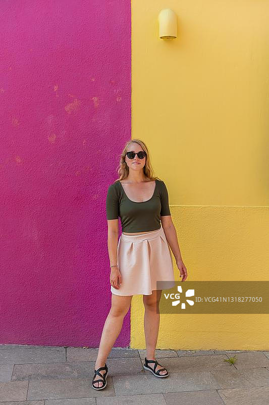 在彩色房子前欢笑的连衣裙年轻女子，黄色和粉色的房子外墙，布拉诺岛，威尼斯，韦内托，意大利图片素材