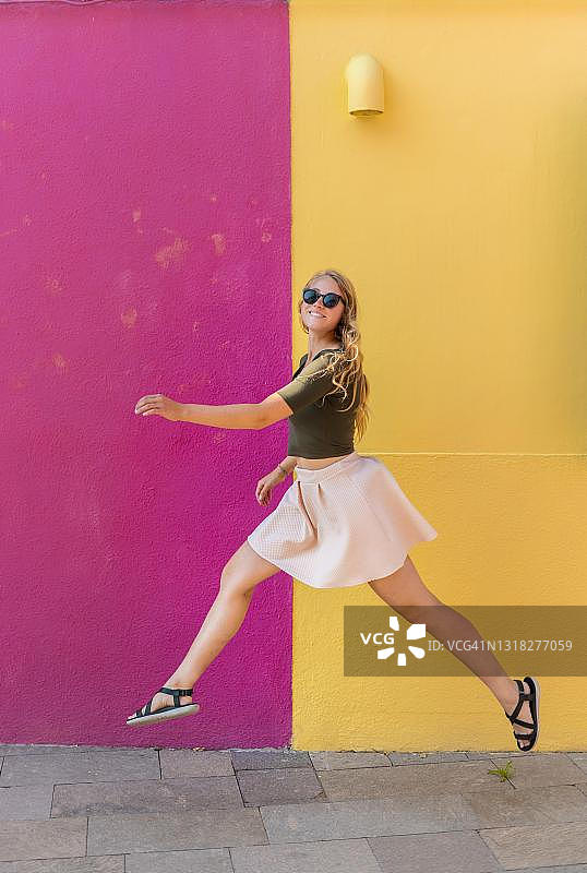 在威尼斯的布拉诺岛，色彩缤纷的房子前快乐跳跃的年轻女子图片素材