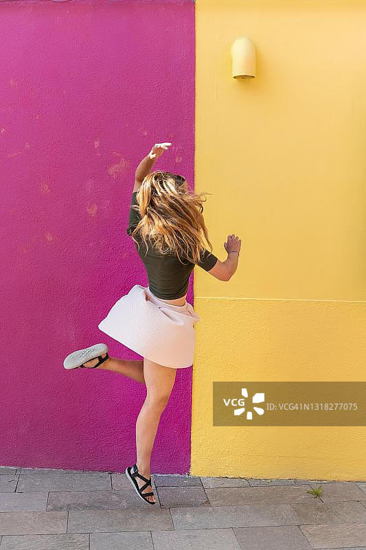 在威尼斯的布拉诺岛，色彩缤纷的房子前快乐跳跃的年轻女子图片素材