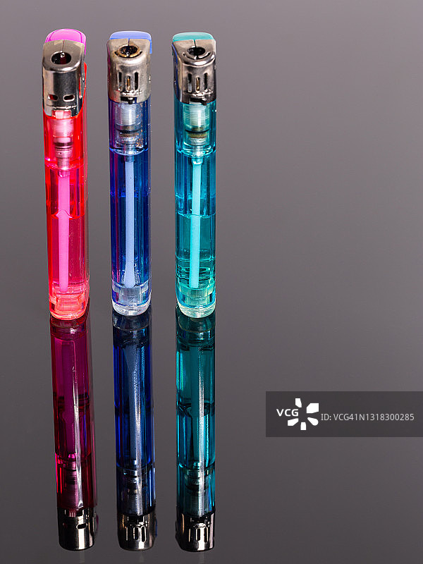 灰色反光背景上不同颜色的三个气体打火机图片素材