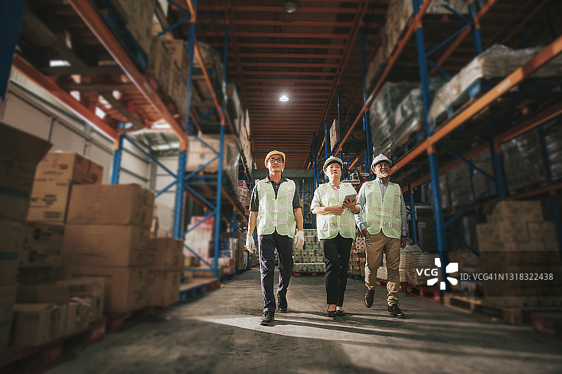 华人管理层与仓库工人在仓库讨论，工人戴着白色安全帽，使用数字平板电脑图片素材