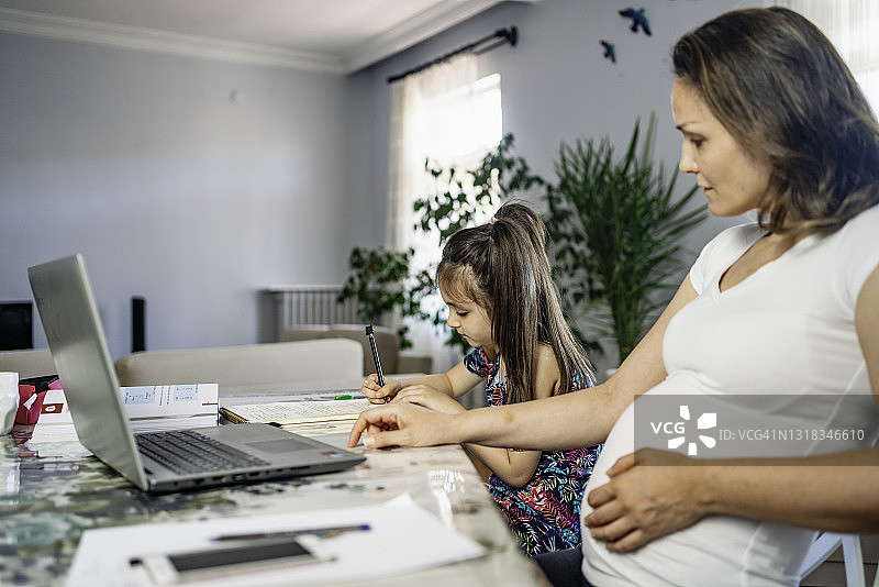 新冠疫情期间的家庭教育：年轻孕妇在家庭氛围中辅导十几岁的女儿做作业，家庭生活方式图片素材
