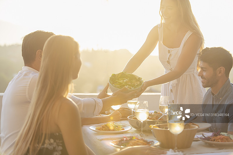 朋友和家人在日落时分在桌子上分沙拉图片素材