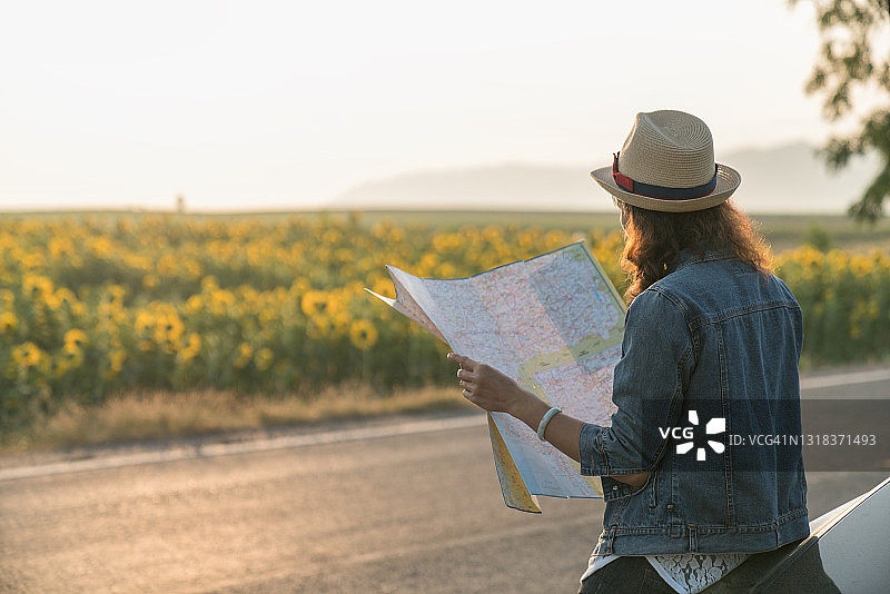 旅行女孩在地图上寻找正确方向的背面，明亮的橙色日落光，在欧洲旅行，自由和积极的生活方式概念图片素材