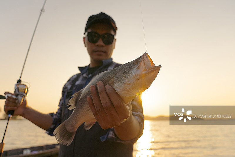 快乐的垂钓者展示鲈鱼渔获图片素材