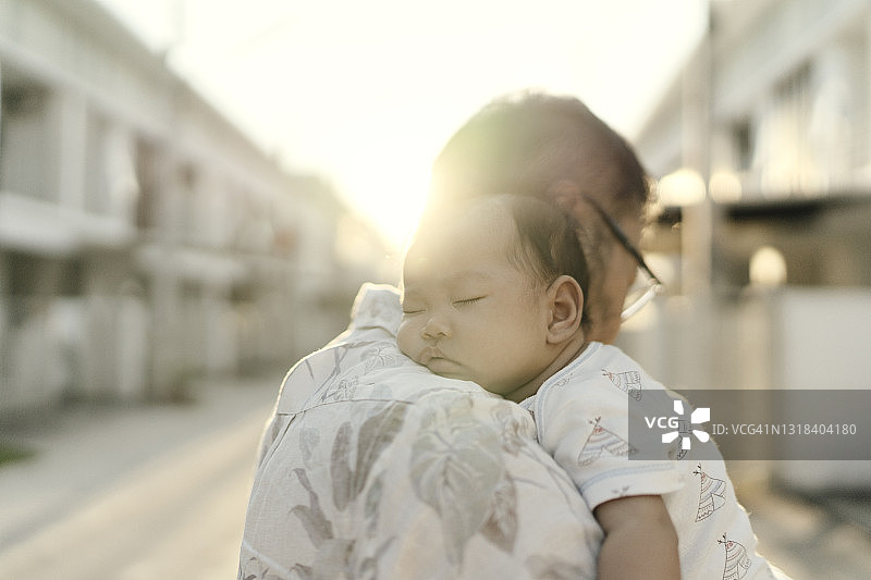 亚裔单身父亲在日落时拥抱熟睡的女儿图片素材