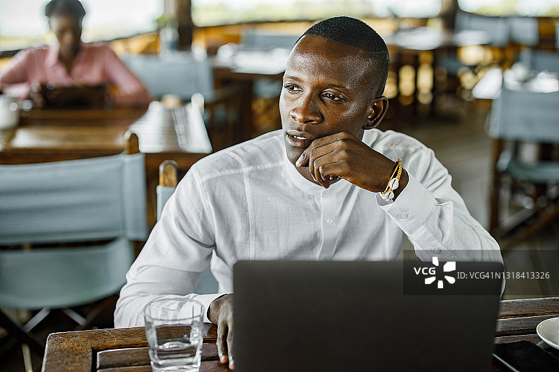 在咖啡馆用笔记本电脑工作的沉思的黑人商人图片素材