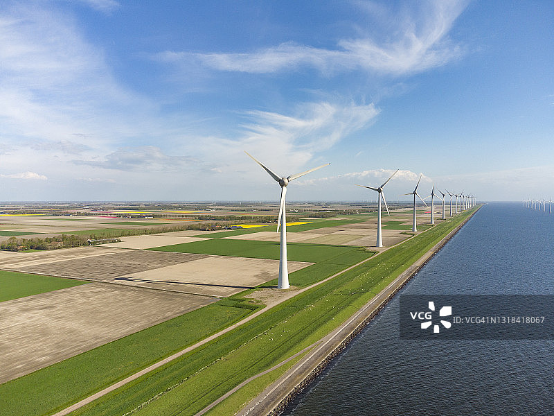 堤坝上的风力涡轮机，背景是农田和湖泊图片素材