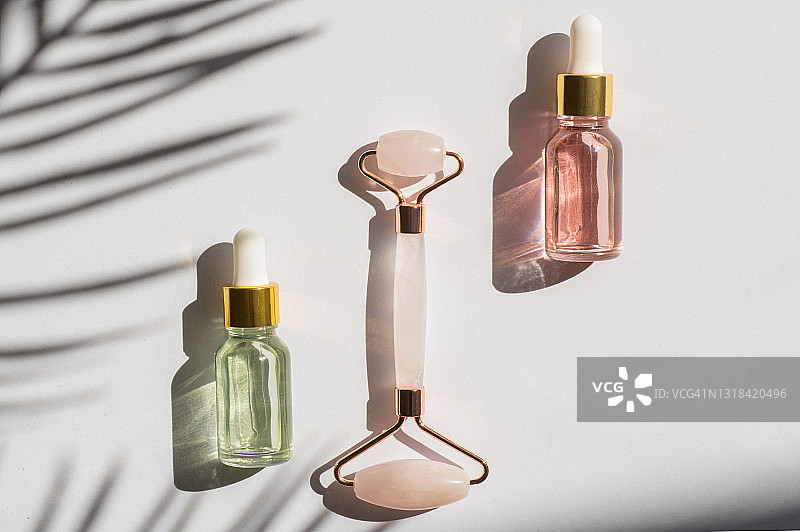 美容工具：瓜痧滚轮与热带树叶阴影和面部护理精华液图片素材