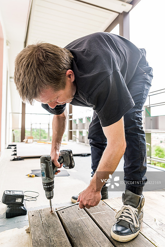 男人用充电螺丝刀从露台上拆除旧木板图片素材