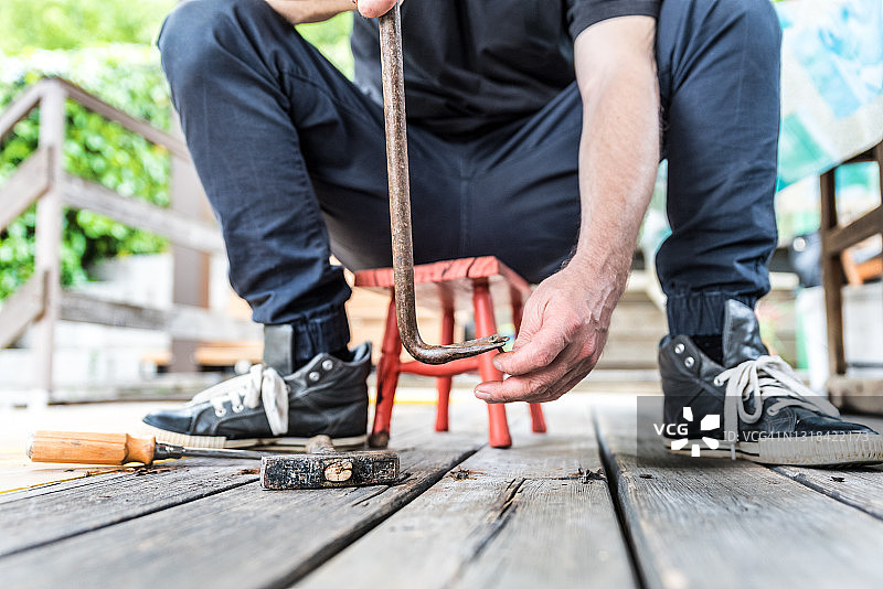 男人用撬棍从露台上移走旧木板图片素材
