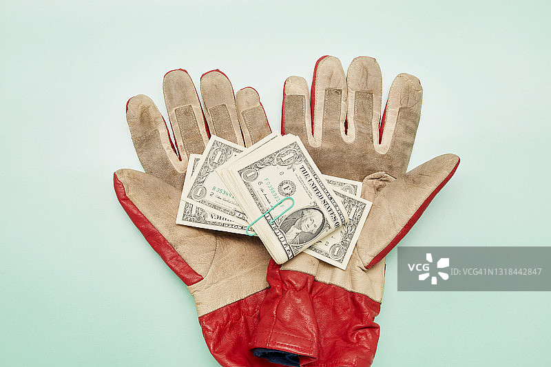 绿松石背景上的工作手套和美元纸币高角度视图图片素材