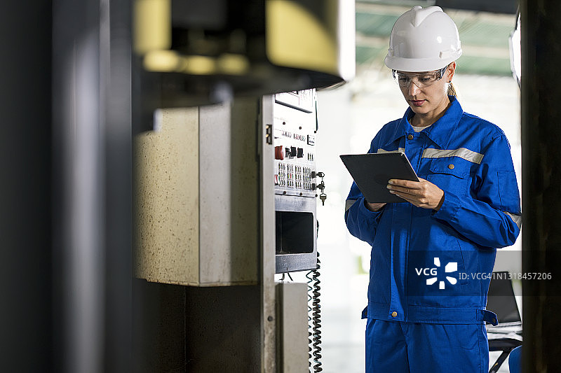 女工程师在数字平板电脑上操作CNC铣床，她是通过使用基于PC的控制集成机床的所有功能的机械工程专家图片素材