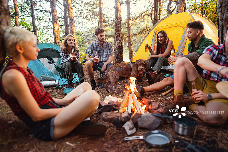 快乐的年轻露营者在篝火旁喝啤酒图片素材