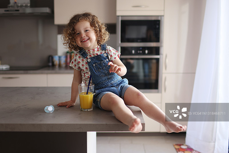 2岁女孩在厨房喝橙汁图片素材