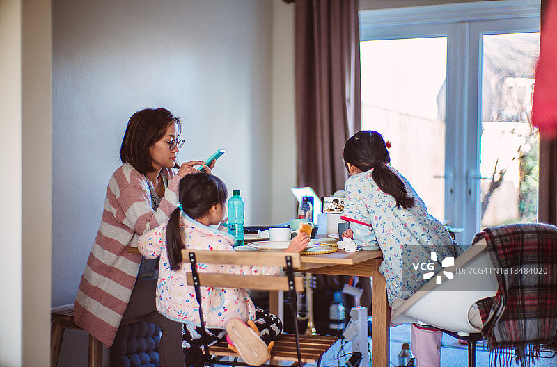 可爱的小姐妹在妈妈用智能手机的时候，通过视频电话和朋友们进行虚拟早餐图片素材