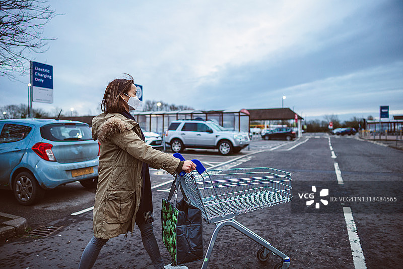 戴防护口罩的年轻亚洲女性在黄昏时推着空购物车图片素材