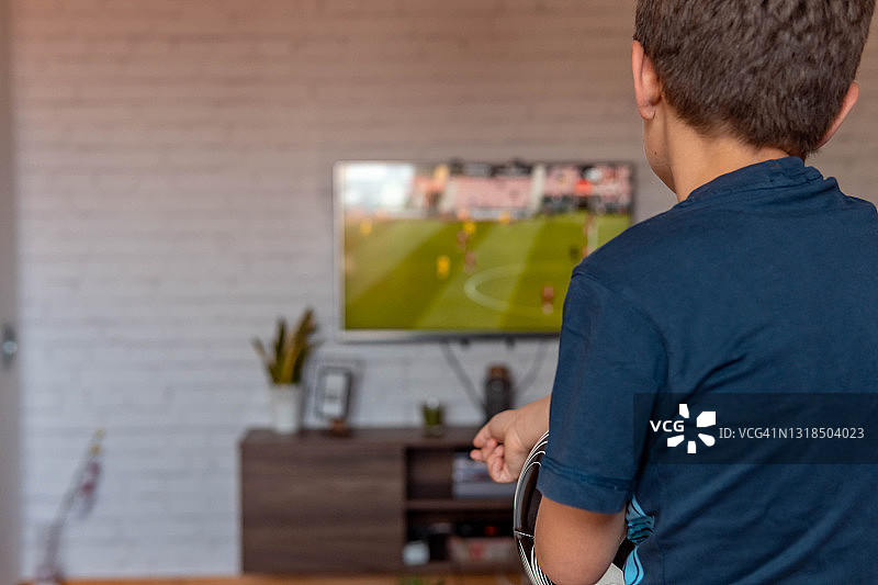后视图：男孩在家看电视，观看足球比赛图片素材