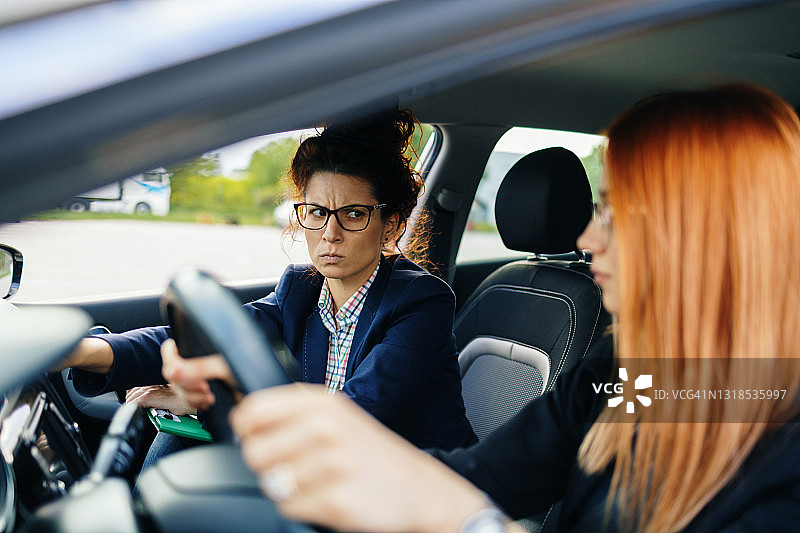 驾校或考试。美丽的年轻女人和她的教练一起学习如何开车。图片素材