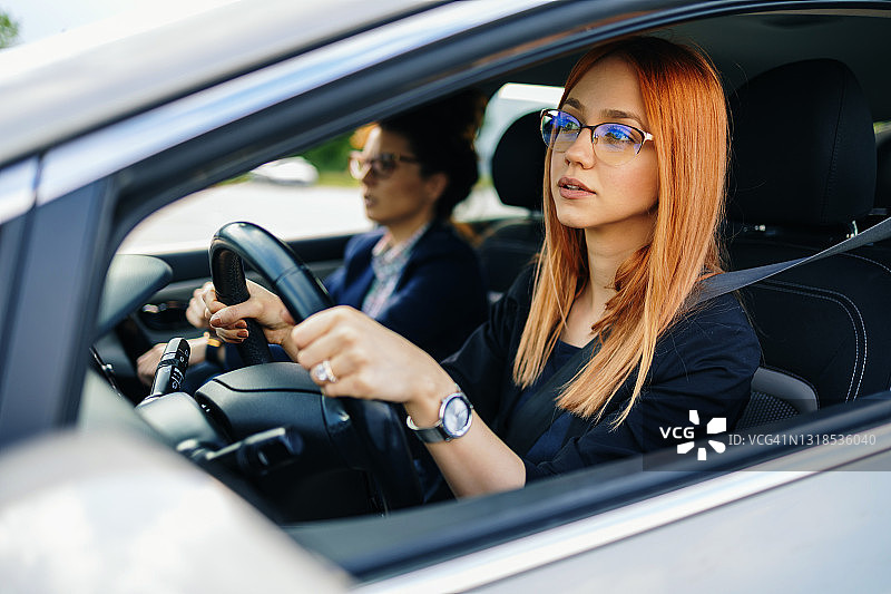 驾校或考试。美丽的年轻女人和她的教练一起学习如何开车。图片素材