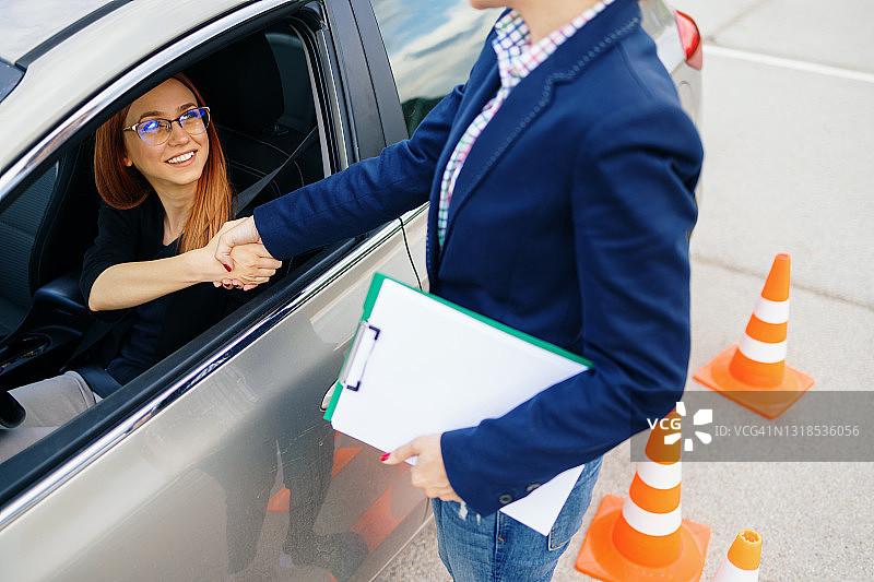 驾校或考试。美丽的年轻女人和她的教练一起学习如何开车。图片素材