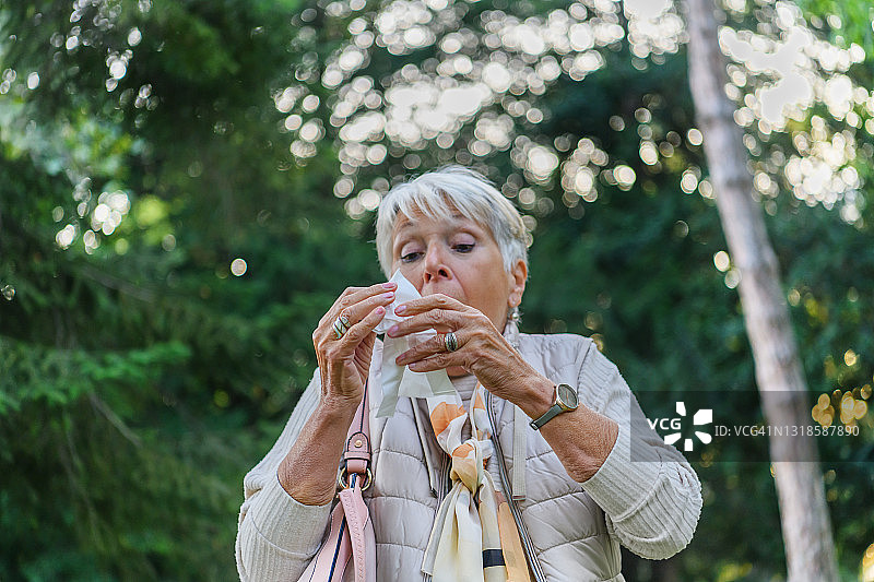 患有季节性过敏症的年长妇女正在用纸巾擤鼻涕图片素材