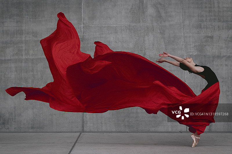 在灰色水泥墙前跳舞的女芭蕾舞演员，脚尖有红色面纱图片素材