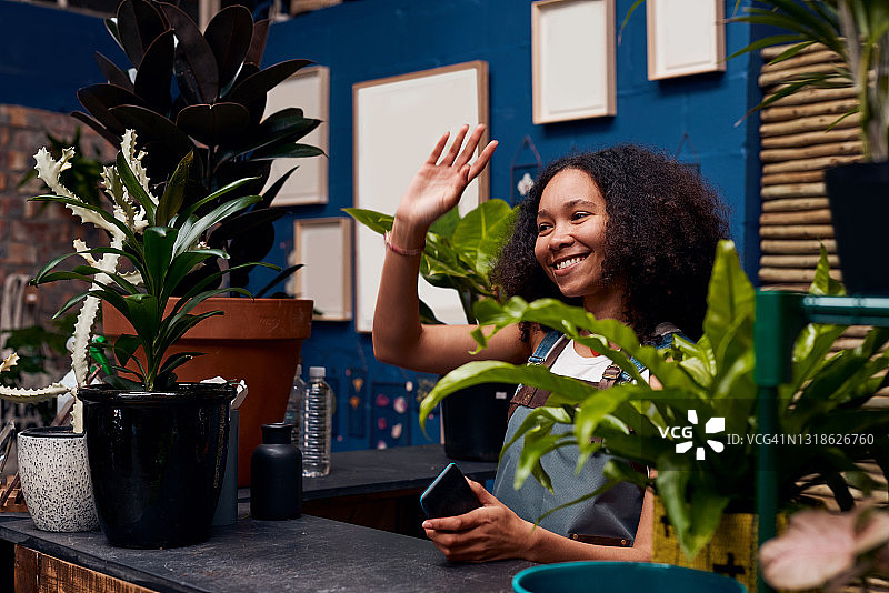 年轻女人站在园艺中心柜台后挥手图片素材