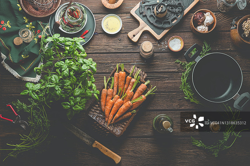 复古烤盘中成堆的橙色胡萝卜、罗勒、香料、食材和烹饪设备，在乡村木制厨房桌子上图片素材
