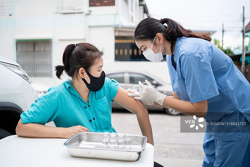 驾车接种疫苗点，亚洲年轻医生为驾车人士注射新冠疫苗图片素材