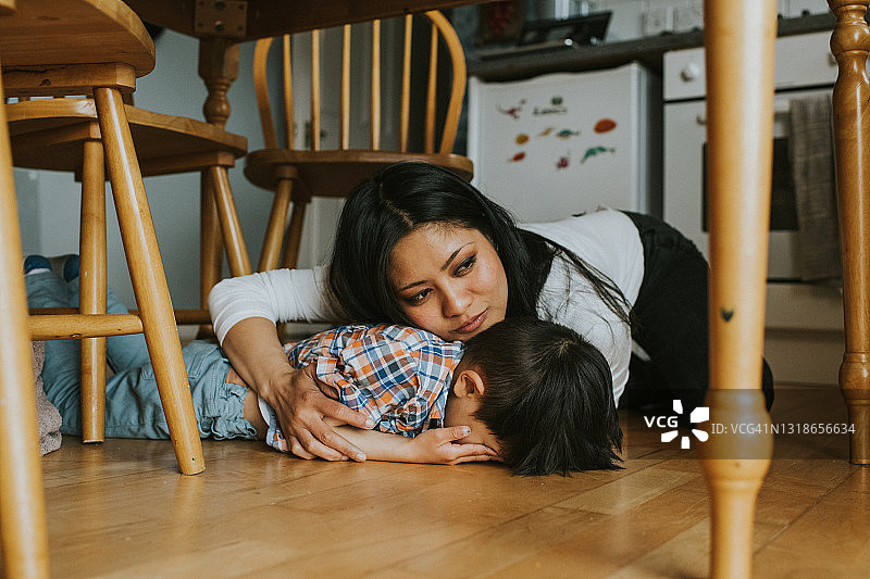 小男孩趴在桌子下的地板上，一位女士正在安慰他图片素材
