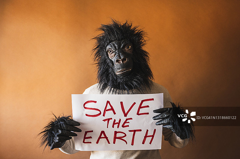 打扮成大猩猩的男人举着写着“拯救地球”的纸板标志图片素材