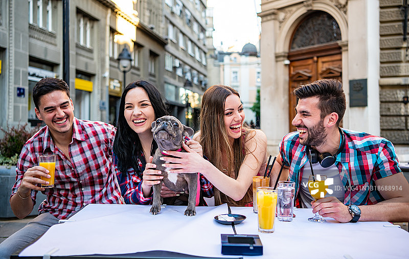 时尚潮人朋友在桌旁喝酒，快乐女孩抱着可爱的小狗图片素材