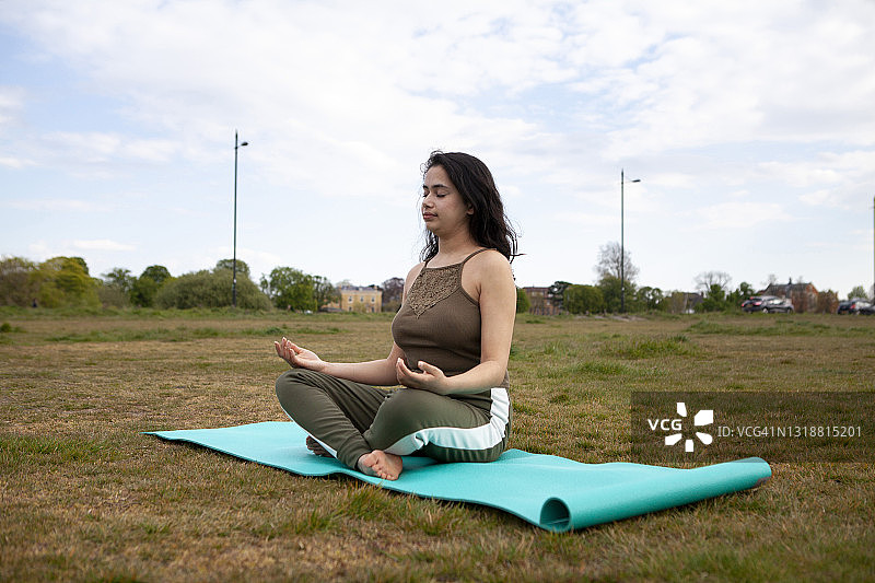 年轻女子在公园的瑜伽垫上做瑜伽图片素材