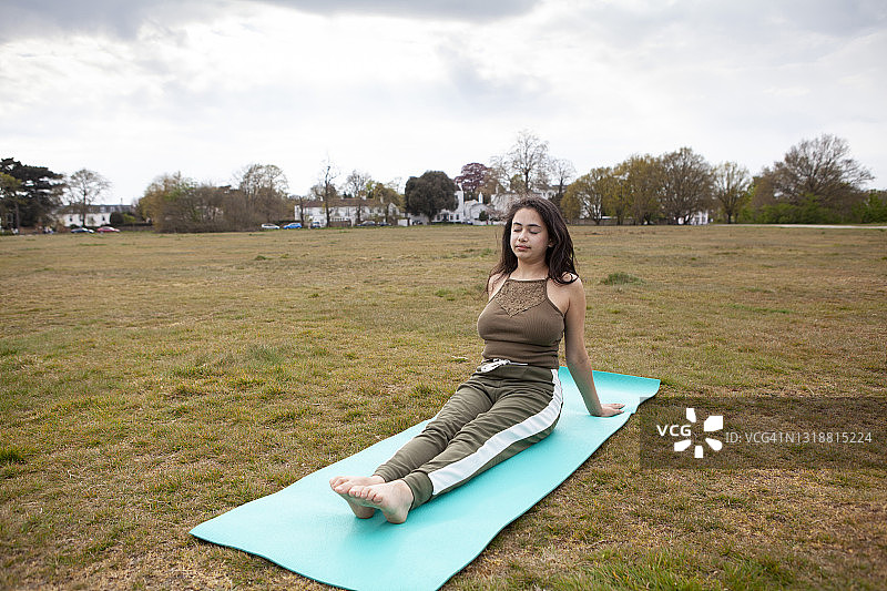 年轻女人在公园的蓝绿色垫子上闭目练习瑜伽图片素材