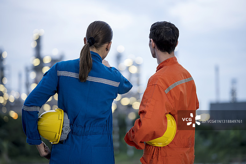 在工业区石油炼油厂，石化工程师在深夜轮班时讨论生产计划的背影。石化制造业。图片素材