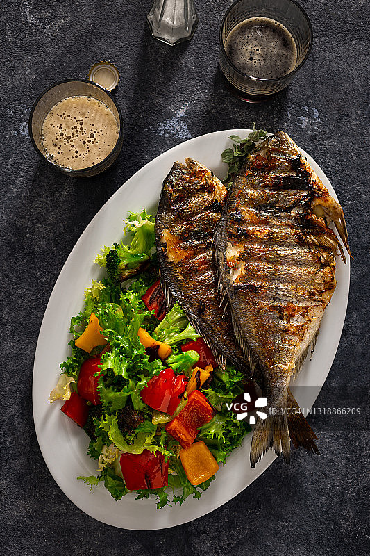 深色背景下炸多拉多鱼和新鲜沙拉拼盘，顶视图配黑啤酒图片素材