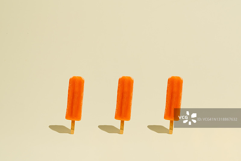 黄色背景上的三根橙味冰棒图片素材