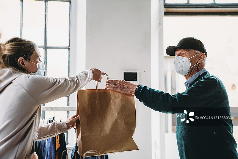 年长的男人在食物和衣物银行领取装有食物和饮料的纸袋图片素材