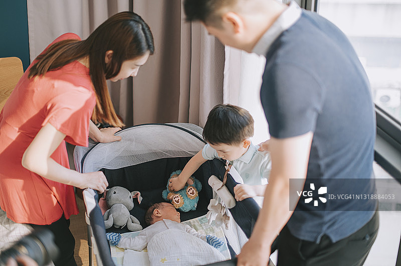 亚洲华人男孩在卧室里与父母一起触摸婴儿床里的弟弟图片素材