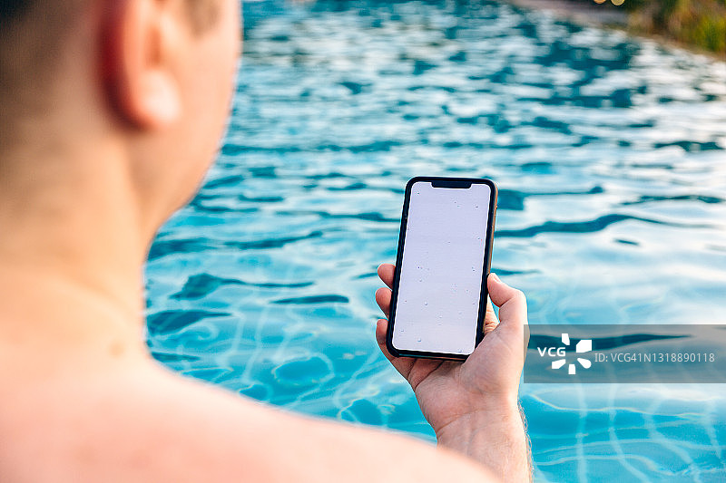 男子在游泳池中使用智能手机图片素材